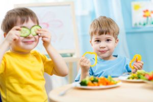 two toddler boys sitting at a table eating vegetables