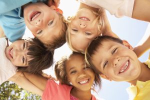 group of children standing in circle with arms around each other looking down into the camera