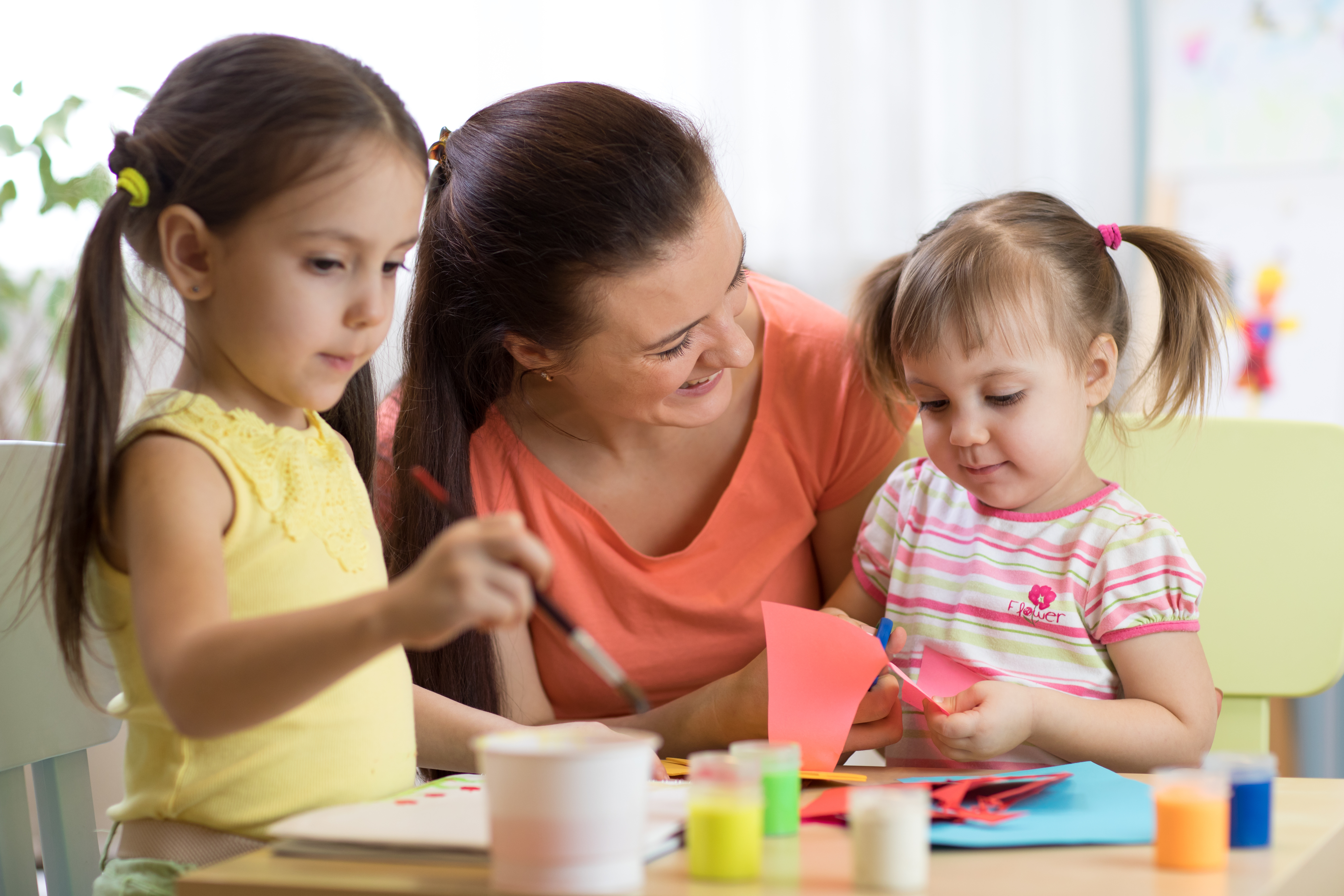 woman sitting with and smiling at two young girls as they do arts and crafts