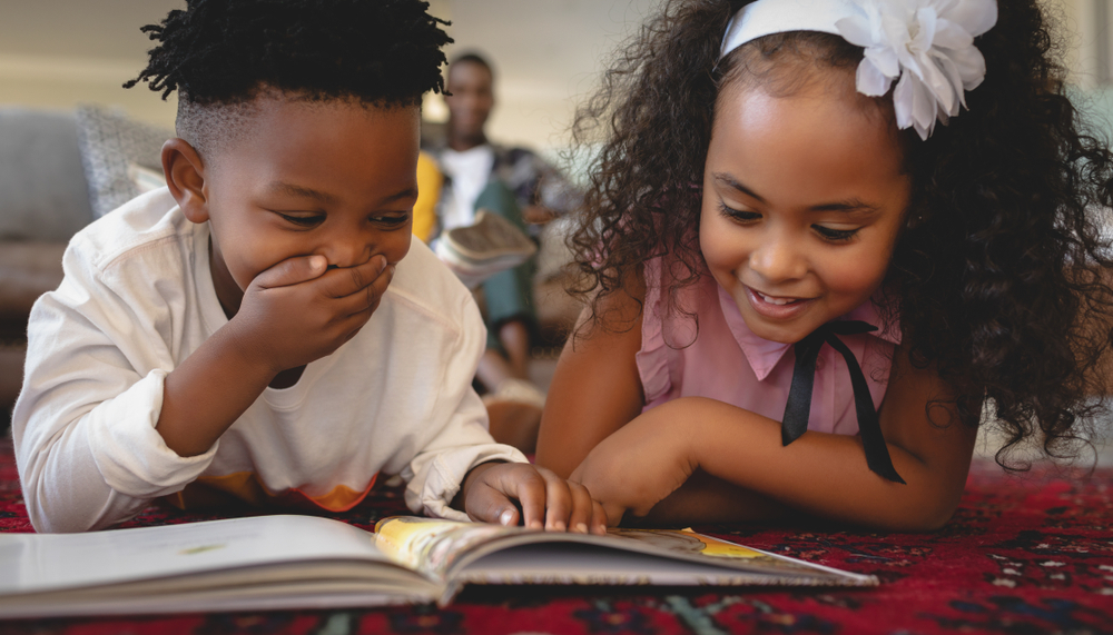 two kids reading a book and laughing 